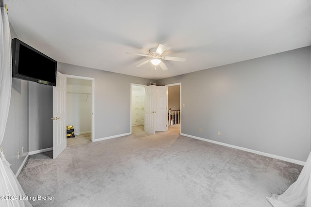 unfurnished bedroom featuring baseboards, a ceiling fan, light carpet, and a spacious closet