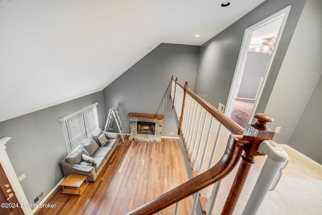 stairway with wood finished floors, a warm lit fireplace, visible vents, a ceiling fan, and lofted ceiling