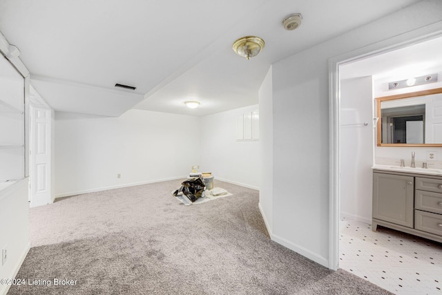 finished below grade area featuring visible vents, light carpet, baseboards, and a sink