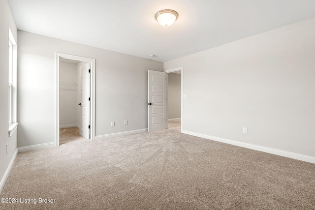 unfurnished bedroom with baseboards, light carpet, a walk in closet, and a closet