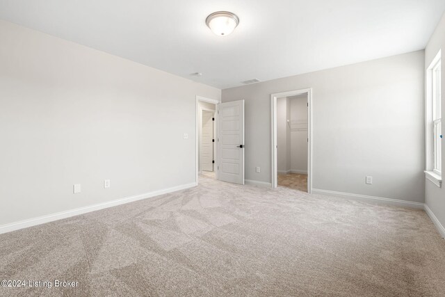 unfurnished bedroom with baseboards, visible vents, a walk in closet, and carpet flooring