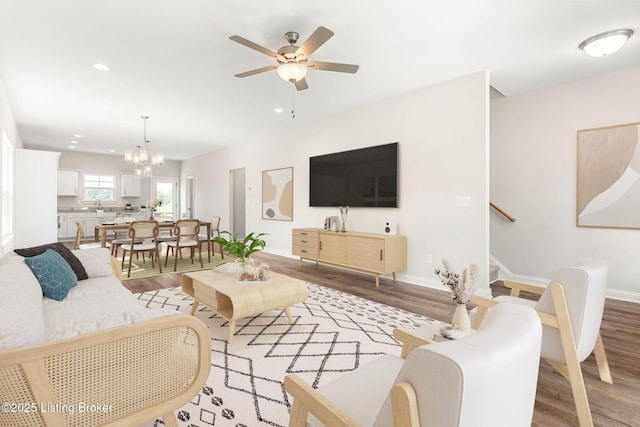 living area featuring baseboards, stairway, wood finished floors, and ceiling fan with notable chandelier