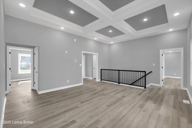 empty room featuring coffered ceiling, light wood-style flooring, beamed ceiling, and baseboards