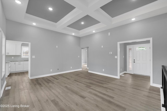 unfurnished living room featuring light wood-style floors, baseboards, and coffered ceiling