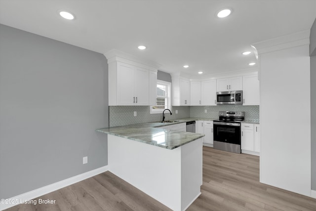 kitchen featuring a sink, decorative backsplash, light stone counters, white cabinets, and appliances with stainless steel finishes