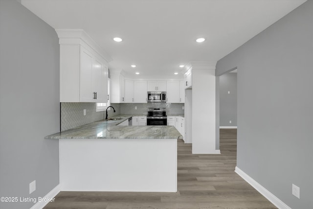 kitchen featuring light stone countertops, tasteful backsplash, stainless steel appliances, a sink, and white cabinetry