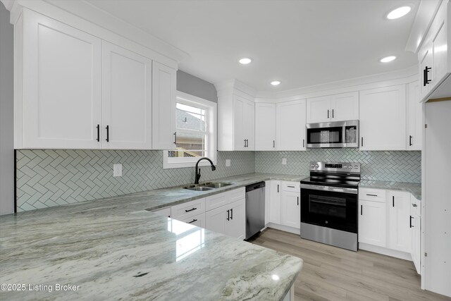 kitchen featuring tasteful backsplash, light stone counters, stainless steel appliances, a sink, and white cabinetry