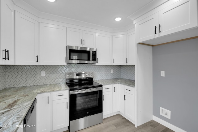 kitchen with white cabinets, appliances with stainless steel finishes, decorative backsplash, and light wood-style floors