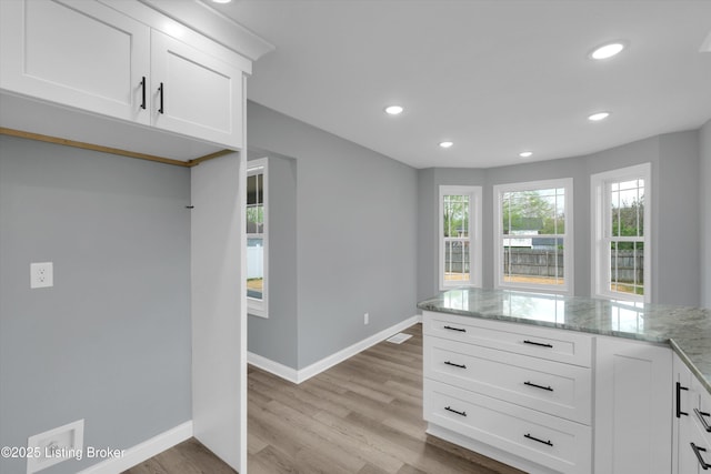 kitchen with white cabinetry, light stone countertops, light wood finished floors, and baseboards