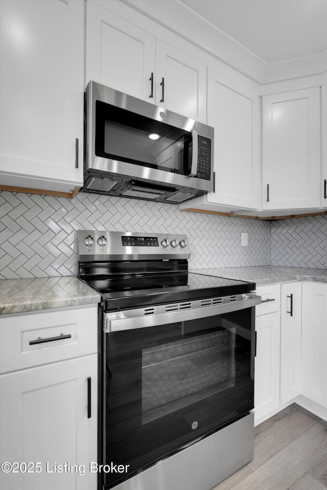 kitchen with light stone countertops, decorative backsplash, stainless steel appliances, light wood finished floors, and white cabinetry