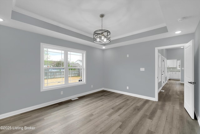 empty room featuring ornamental molding, dark wood-style floors, an inviting chandelier, and a raised ceiling