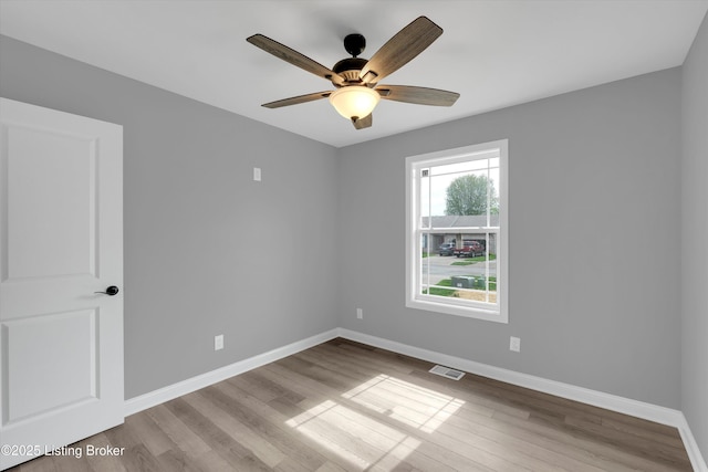 spare room featuring a ceiling fan, visible vents, wood finished floors, and baseboards