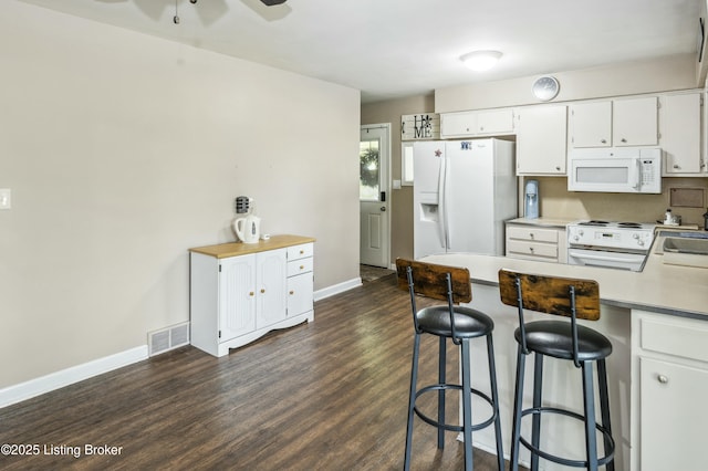 kitchen featuring dark wood-style flooring, white appliances, visible vents, baseboards, and white cabinets