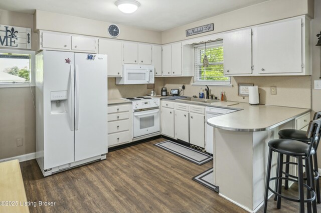 kitchen featuring white appliances, a peninsula, dark wood-type flooring, and a sink