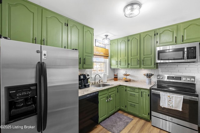 kitchen with stainless steel appliances, green cabinets, backsplash, light wood finished floors, and a sink