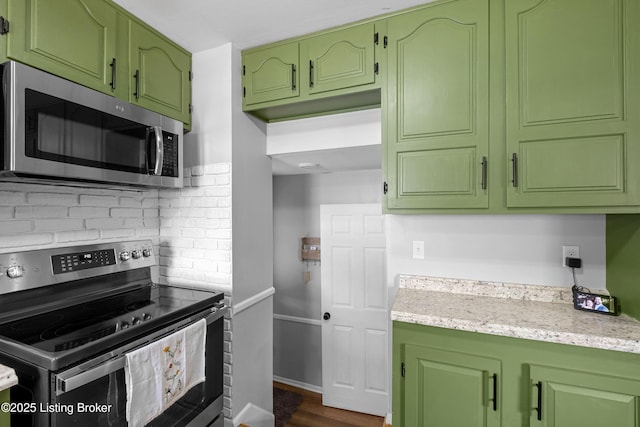 kitchen featuring tasteful backsplash, stainless steel appliances, green cabinets, light stone countertops, and dark wood-type flooring