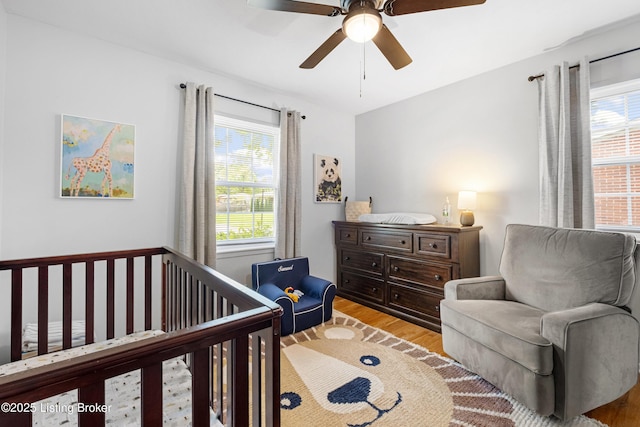 bedroom with a crib, wood finished floors, a ceiling fan, and multiple windows