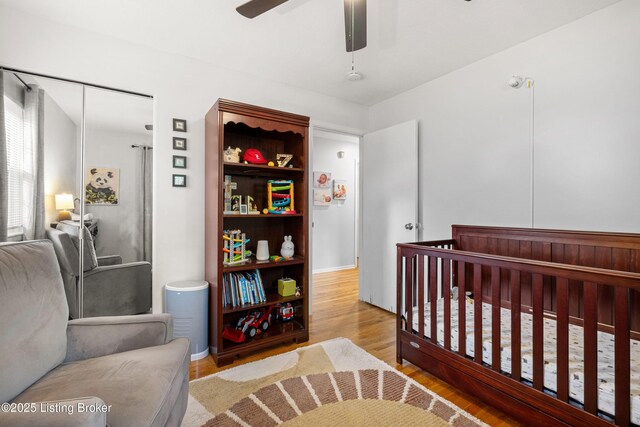 bedroom featuring wood finished floors, ceiling fan, and a nursery area