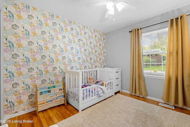 bedroom with wood finished floors, visible vents, wallpapered walls, and a nursery area
