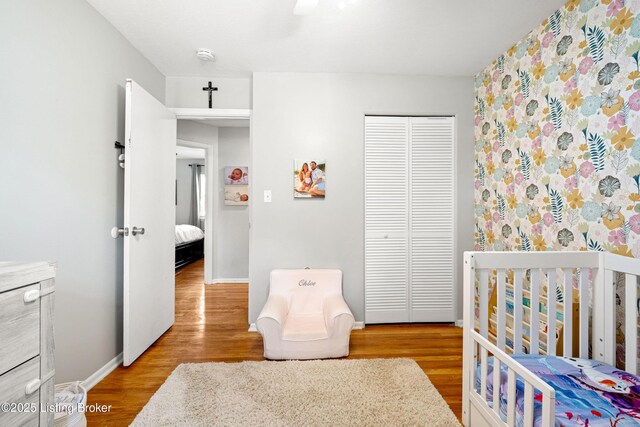 bedroom featuring wood finished floors, baseboards, a nursery area, and a closet