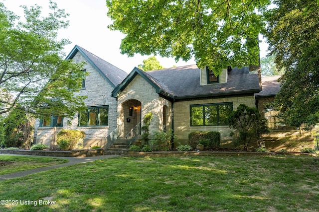 tudor house with a front lawn, stone siding, and roof with shingles