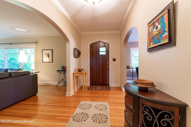 foyer featuring light wood-style floors, baseboards, ornamental molding, and arched walkways