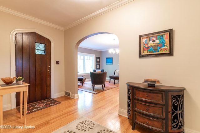 entrance foyer with an inviting chandelier, light wood-style floors, crown molding, baseboards, and arched walkways