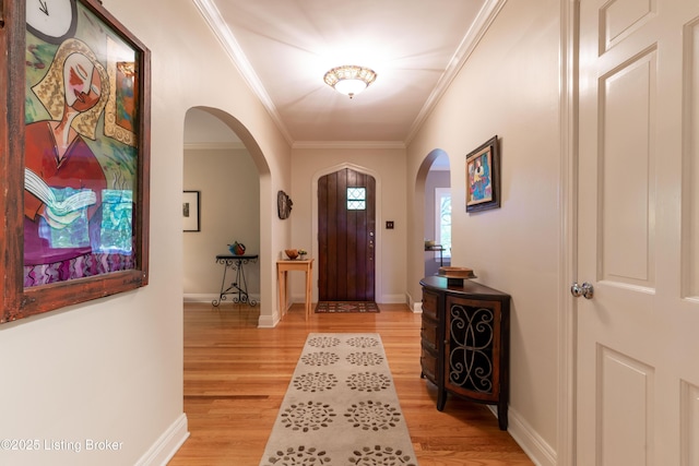 foyer entrance with crown molding, arched walkways, baseboards, and light wood-style floors