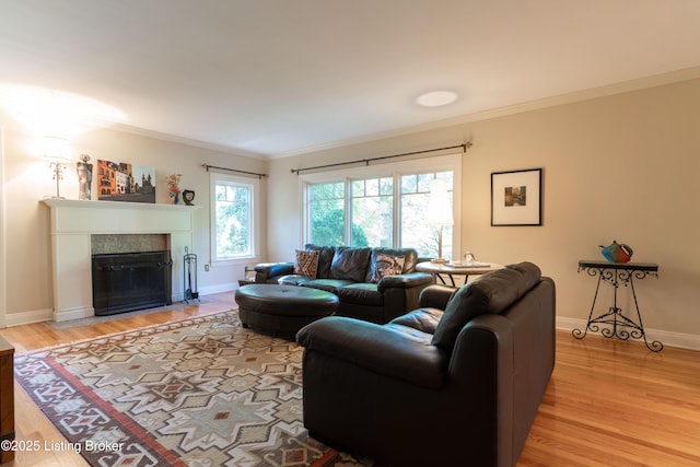 living room featuring ornamental molding, light wood finished floors, a tiled fireplace, and baseboards