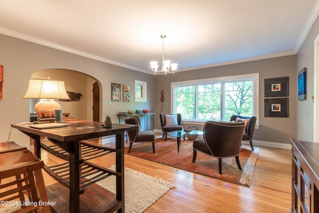 dining area featuring an inviting chandelier, crown molding, light wood-style flooring, and arched walkways
