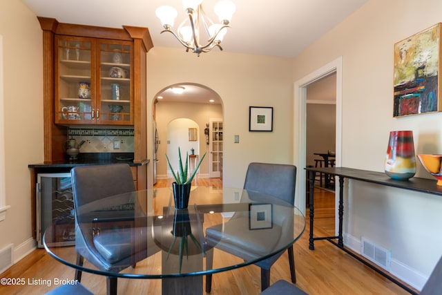 dining room with a chandelier, visible vents, arched walkways, and wood finished floors