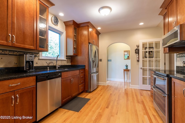 kitchen featuring a sink, tasteful backsplash, light wood-style flooring, arched walkways, and appliances with stainless steel finishes