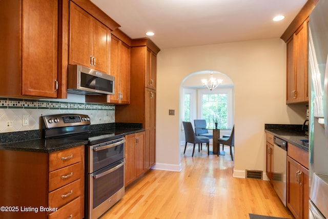 kitchen featuring brown cabinetry, light wood finished floors, an inviting chandelier, and stainless steel appliances