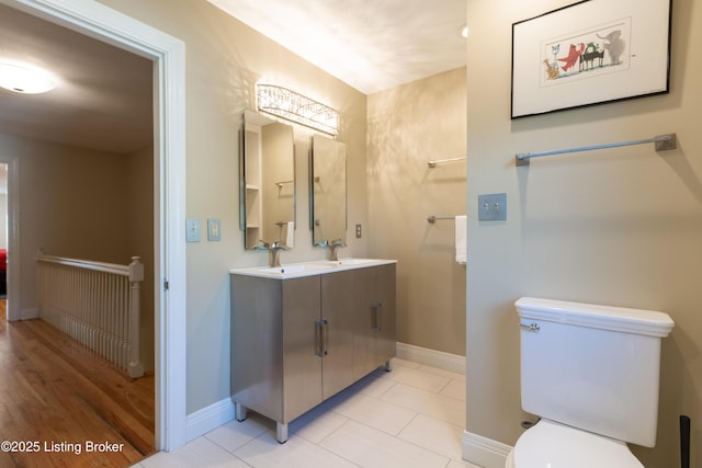 bathroom featuring toilet, double vanity, a sink, and baseboards