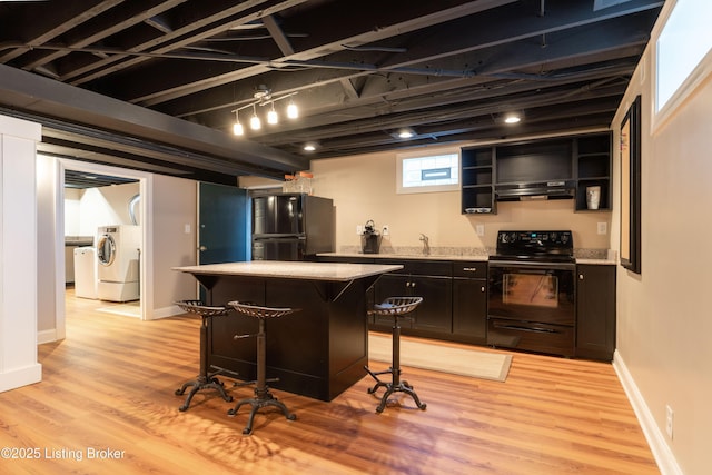 bar featuring under cabinet range hood, black appliances, a sink, light wood-type flooring, and washer / clothes dryer