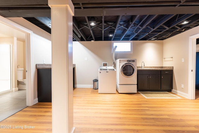 laundry area with light wood-style flooring, washing machine and clothes dryer, a sink, baseboards, and indoor bar