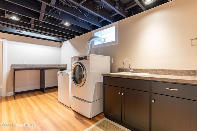clothes washing area with washing machine and dryer, light wood finished floors, and a sink