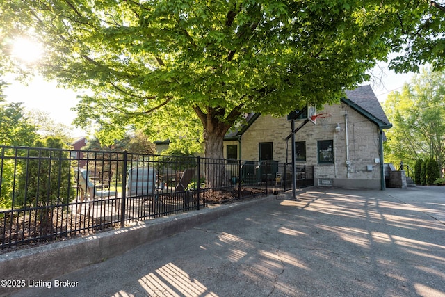view of property hidden behind natural elements featuring fence and stone siding