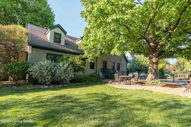 rear view of property featuring a patio, a yard, stone siding, and fence