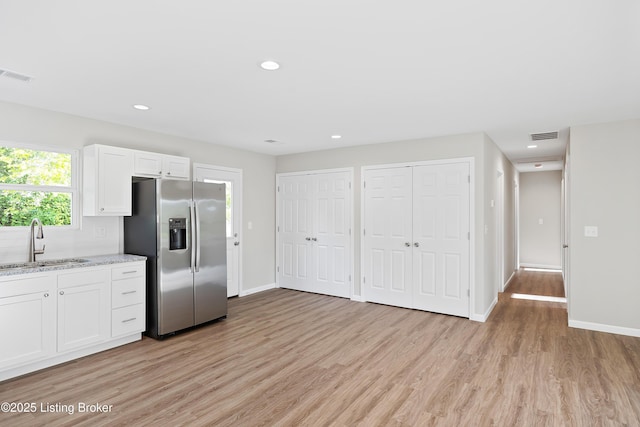 kitchen with visible vents, a sink, stainless steel fridge with ice dispenser, light wood finished floors, and white cabinetry
