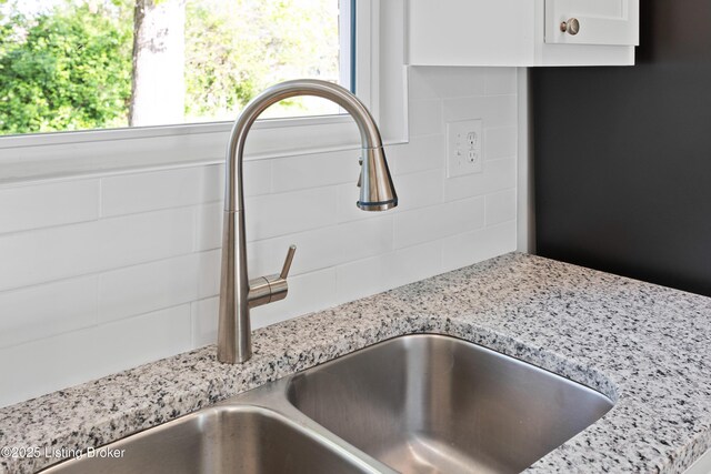 interior details with a sink, light stone countertops, and white cabinetry