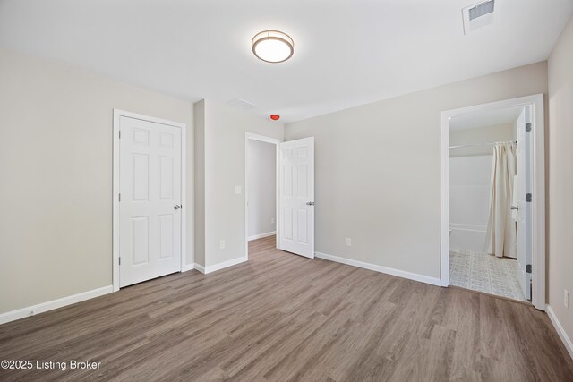 unfurnished bedroom with baseboards, a closet, wood finished floors, and visible vents