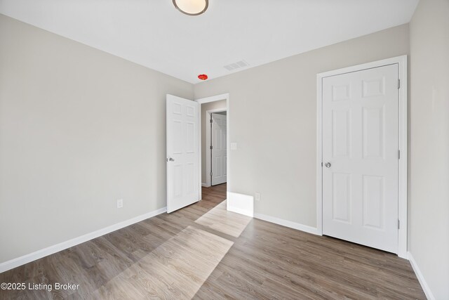 unfurnished bedroom with baseboards, wood finished floors, and visible vents