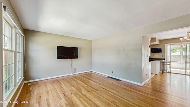 unfurnished living room with light wood-style floors, baseboards, an inviting chandelier, and visible vents