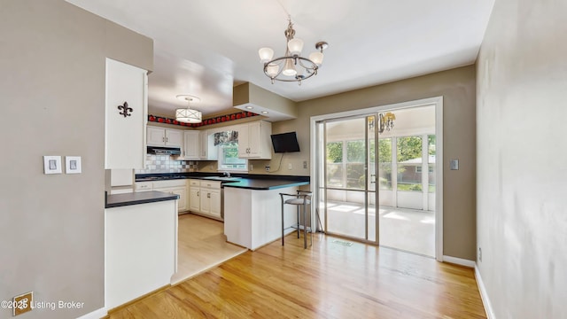 kitchen featuring a wealth of natural light, light wood finished floors, a notable chandelier, and dark countertops