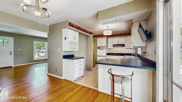 kitchen with dark countertops, a sink, light wood finished floors, backsplash, and white oven