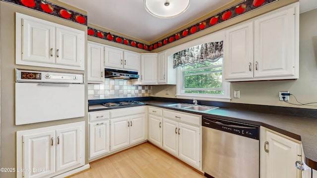 kitchen with dark countertops, a sink, dishwasher, under cabinet range hood, and white oven