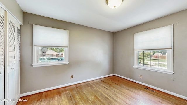 unfurnished bedroom with baseboards, a closet, wood finished floors, and visible vents