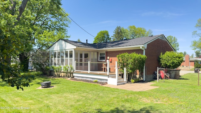 back of house featuring a deck, a sunroom, brick siding, an outdoor fire pit, and a yard