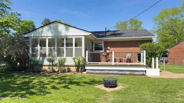 back of house featuring a sunroom, an outdoor fire pit, a lawn, and a deck